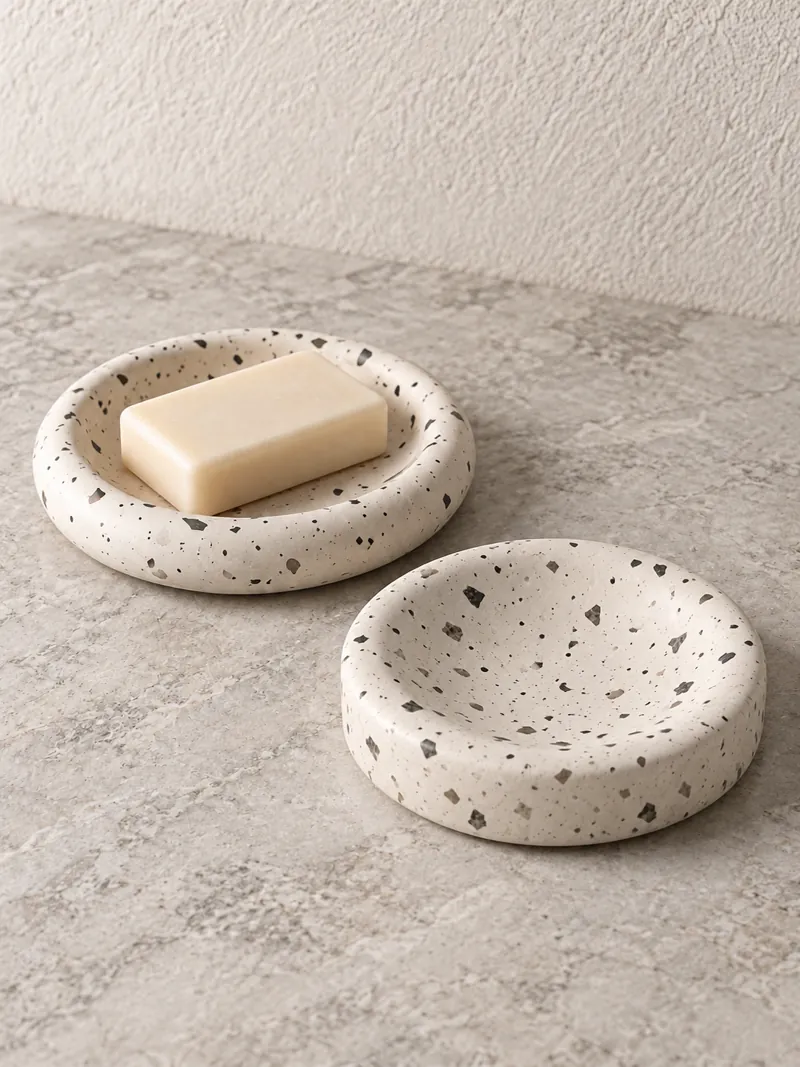 A bar of soap resting on a speckled stone dish beside an empty one.